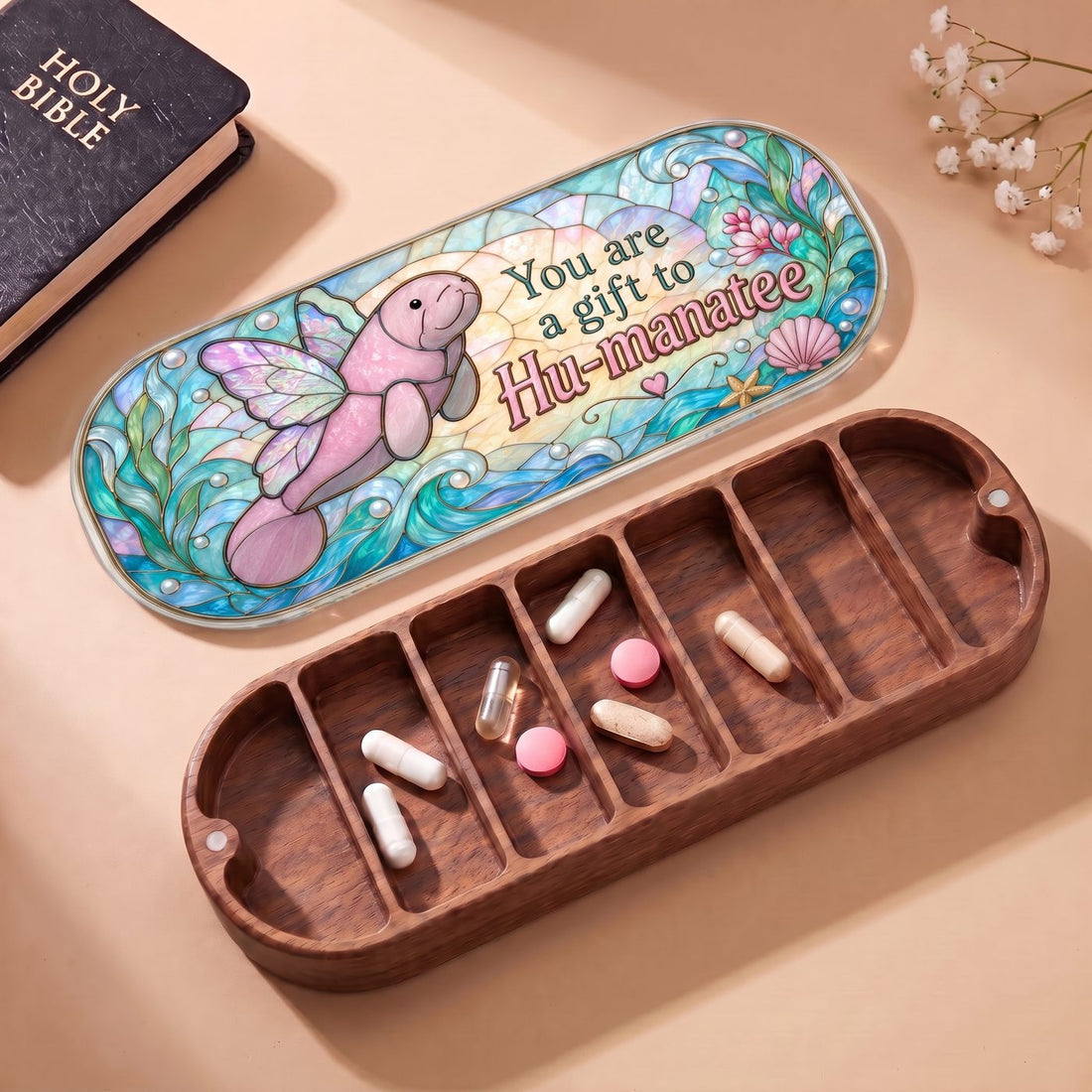 "You Are a Gift to Hu-manatee — Winged Manatee Stained Glass" Pill Case — open Hu-manatee Pill Case with Holy Bible, white flowers, and assorted pills