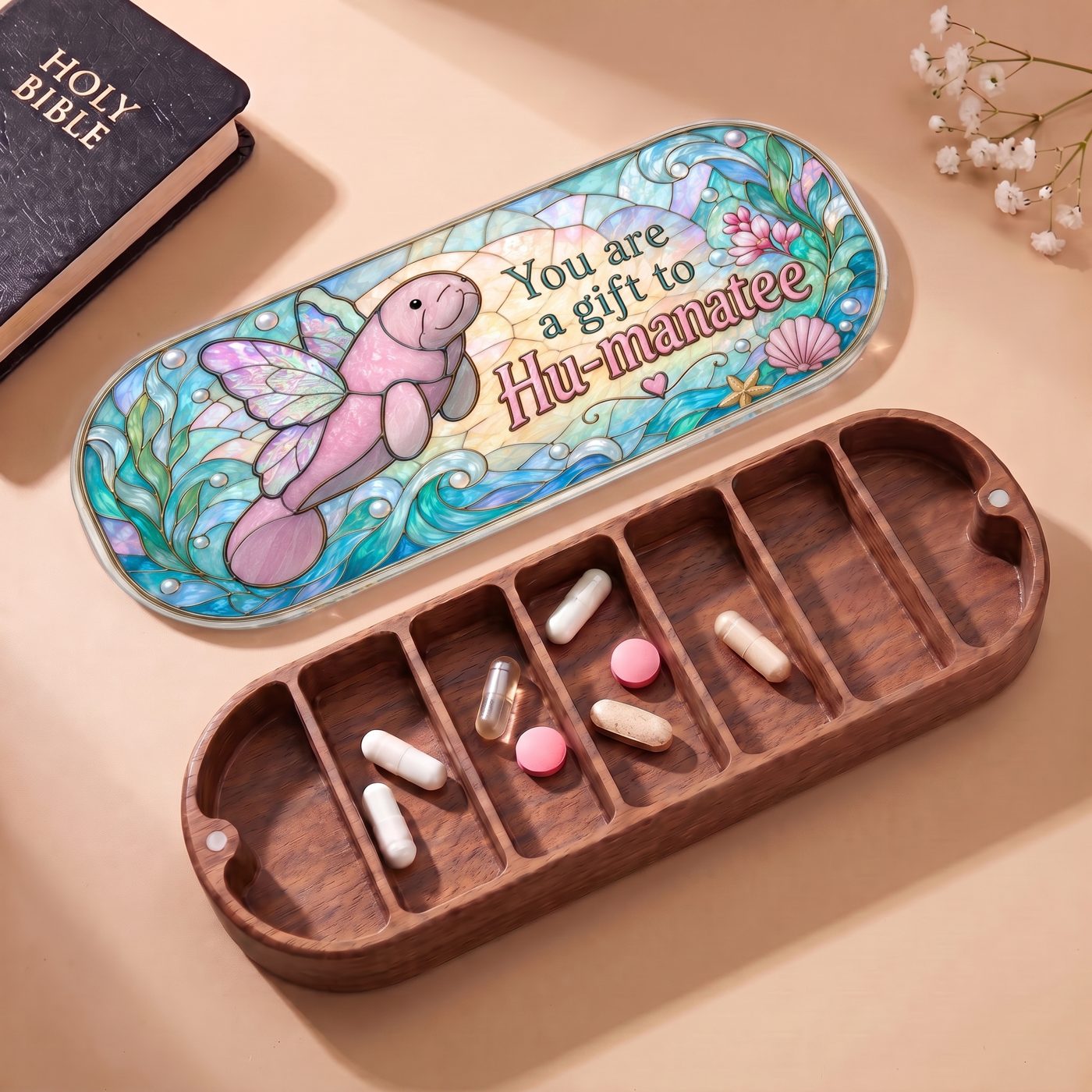 "You Are a Gift to Hu-manatee — Winged Manatee Stained Glass" Pill Case — open Hu-manatee Pill Case with Holy Bible, white flowers, and assorted pills